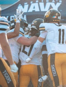 Football players in uniforms celebrate a victory with high fives and hugs on the field.