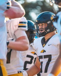 Football players in black helmets and white jerseys during a team huddle on the field.