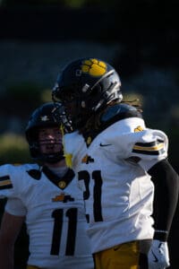Football players in white uniforms with black helmets, number 21, preparing on the field during a game.