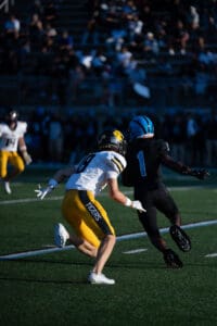 Football players in mid-action on the field during a daytime game, wearing yellow and black uniforms.