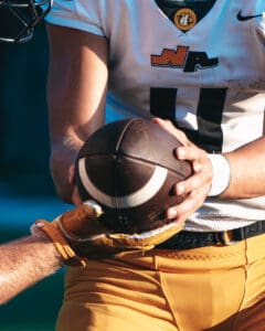 Football player in white jersey holding a football, ready for a pass or handoff during a game.