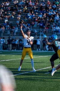 Football player passing ball during a game, in a stadium filled with spectators.