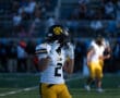 Football player in yellow uniform and helmet with paw logo on field during game.