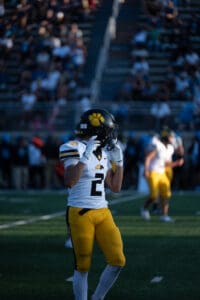 Football player in yellow uniform and helmet with paw logo on field during game.