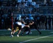 High school football game action with players tackling on the field.