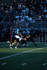 High school football game action with players tackling on the field.