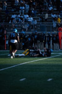 Football players in action during a game with a large crowd in the stands, wearing blue and black uniforms.