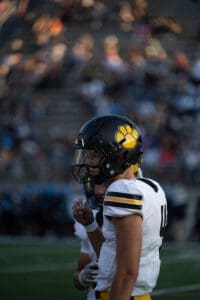 Football player in helmet with yellow paw logo, wearing white jersey, on the field during a game.