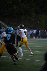 Quarterback in yellow uniform prepares to throw during a football game under stadium lights.