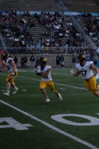 Football players in action on the field, running towards goal, with crowded stands in the background.