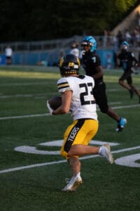 Football player in yellow Tigers uniform running with ball during a game, pursued by opponents.