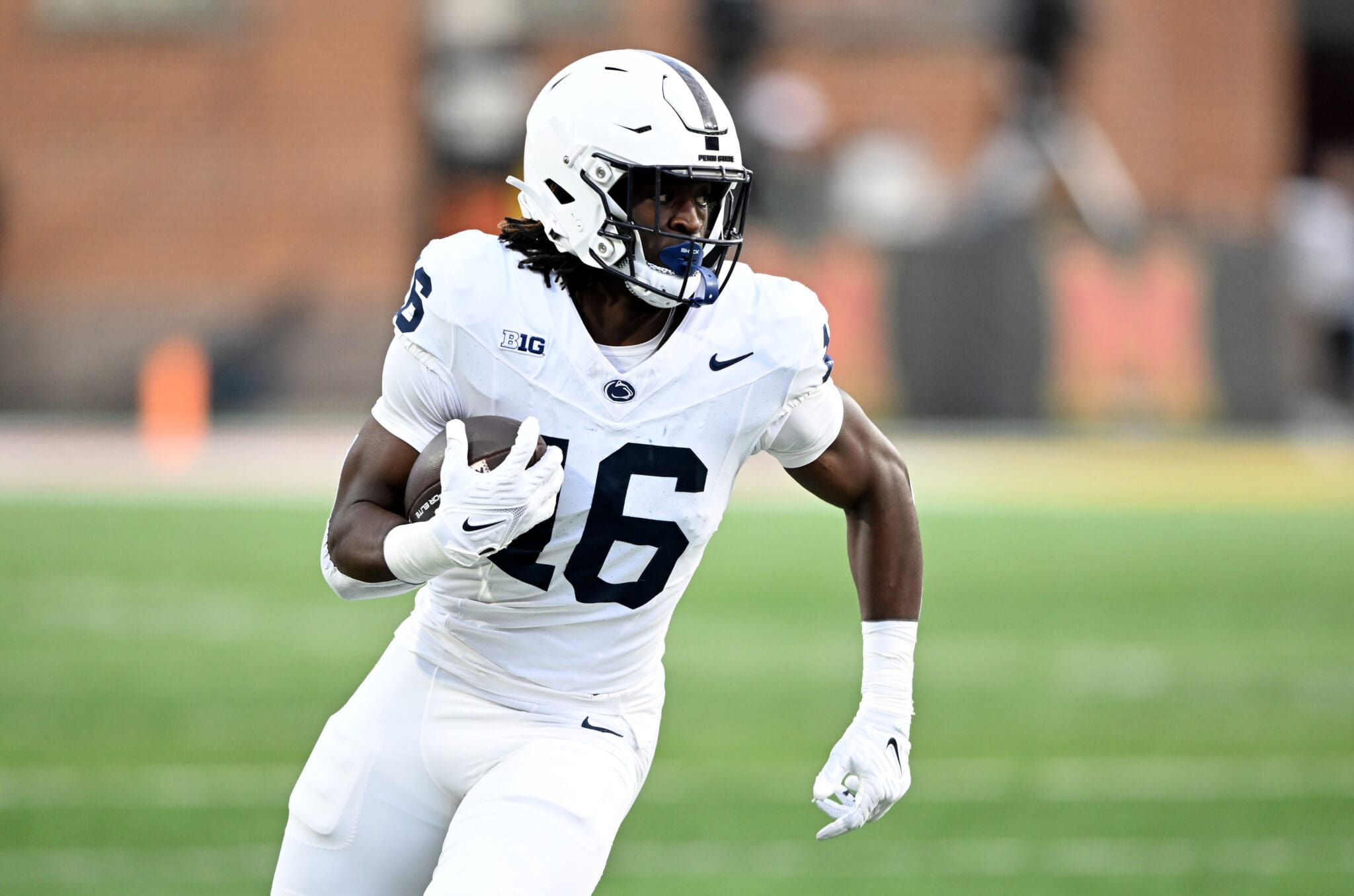 Football player in white uniform running with the ball on a field during a game.