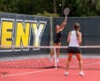 Two women playing a competitive tennis match on a bright red court, one serving the ball.