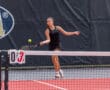Tennis player hitting a forehand shot on a sunny outdoor court during a match.