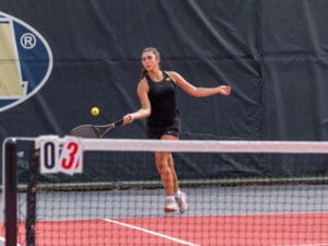 Tennis player hitting a forehand shot on a sunny outdoor court during a match.