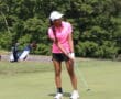 Golfer in pink shirt and white cap putting on a sunny green golf course.