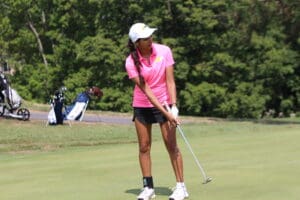 Golfer in pink shirt and white cap putting on a sunny green golf course.