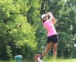 Golfer in pink shirt swings club on lush golf course.
