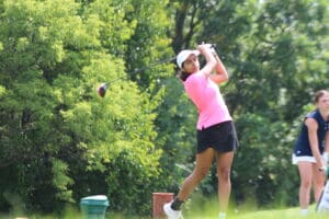Golfer in pink shirt swings club on lush golf course.