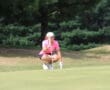 Golfer in pink shirt lining up a putt on a green course, focusing intently with putter in hand.