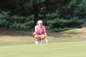 Golfer in pink shirt lining up a putt on a green course, focusing intently with putter in hand.