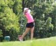 Golfer in pink shirt and black skirt swinging on a lush, green course.