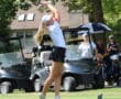 Golfer in mid-swing on a sunny day, surrounded by golf carts and spectators, showcasing a dynamic outdoor golf scene.
