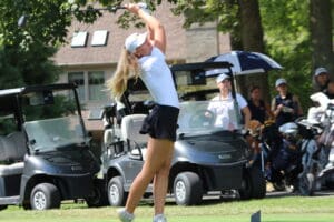Golfer in mid-swing on a sunny day, surrounded by golf carts and spectators, showcasing a dynamic outdoor golf scene.