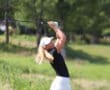Golfer in black shirt and white cap swinging club on sunny day at lush golf course.