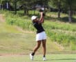Golfer in mid-swing on a lush green course under clear skies, showcasing athletic skill.