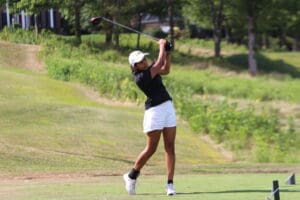 Golfer in mid-swing on a lush green course under clear skies, showcasing athletic skill.