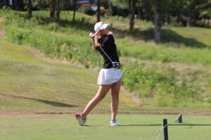 Golfer in mid-swing on a sunny day at a lush green golf course.
