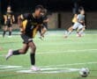 Soccer player in black and yellow jersey dribbles during a match at night, focused on ball control.