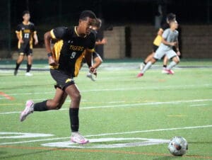 Soccer player in black and yellow jersey dribbles during a match at night, focused on ball control.