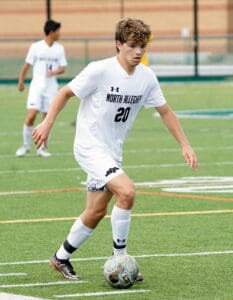 Soccer player dribbling ball on field, wearing North Allegheny jersey, during a match.
