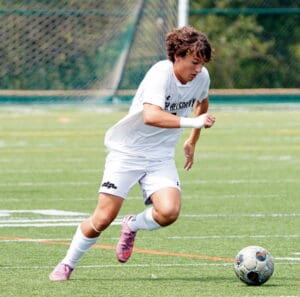 Soccer player in white uniform dribbling a ball on a green field, showcasing athletic skills during a match.
