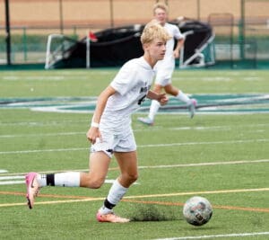 Soccer player in white uniform dribbling ball on field; focus on action and movement.