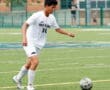 Soccer player in a white uniform dribbling a ball on a field during a game.