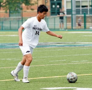 Soccer player in a white uniform dribbling a ball on a field during a game.