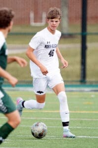 Soccer player in white uniform dribbling ball on field during match, wearing number 46.