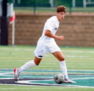 Soccer player in white uniform dribbling ball on field during a match.