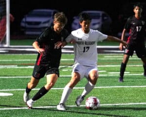 Two soccer players compete for the ball during a night match on a green field.
