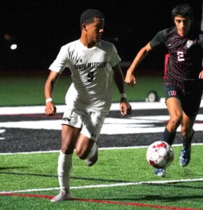 Soccer players in action during a nighttime match, focused on controlling the ball on a lit field.