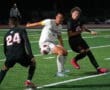 High school soccer match at night, players battling for the ball on the field.