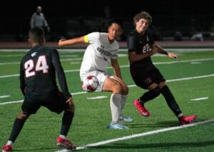 High school soccer match at night, players battling for the ball on the field.