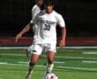 Soccer player in white uniform dribbling soccer ball on field at night game.