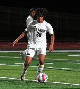 Soccer player in white uniform dribbling soccer ball on field at night game.