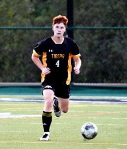 Young soccer player in black and yellow jersey with ball on field during a game.