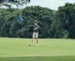 Golfer lining up a putt on a lush green course with trees and a blue checkered flag in the background.