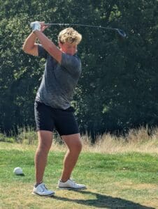 Golfer in mid-swing on a sunny day at the course, surrounded by lush greenery.